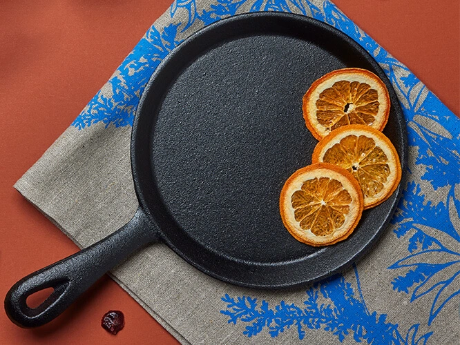 A cast iron pancake pan on a table with a linen tea towel.