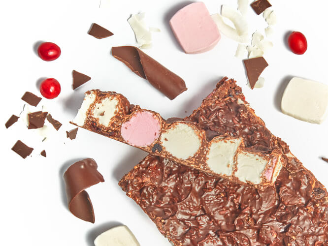 A block of handmade Rocky Road surrounded by ingredients including marshmallow, Belgian Dark chocolate, coconut and cranberries. Shop Rocky Road online at Whisk & Pin.